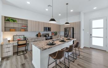 A modern kitchen with a marble countertop and wooden flooring.at Marketside Villas at Verrado, Buckeye, AZ 85396